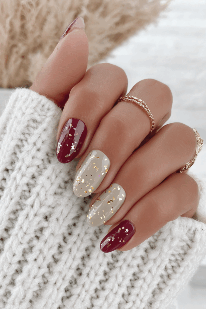 Dark claret red almond nails with a gold flake speckle topcoat on two accent nails for a rich, textured winter look.