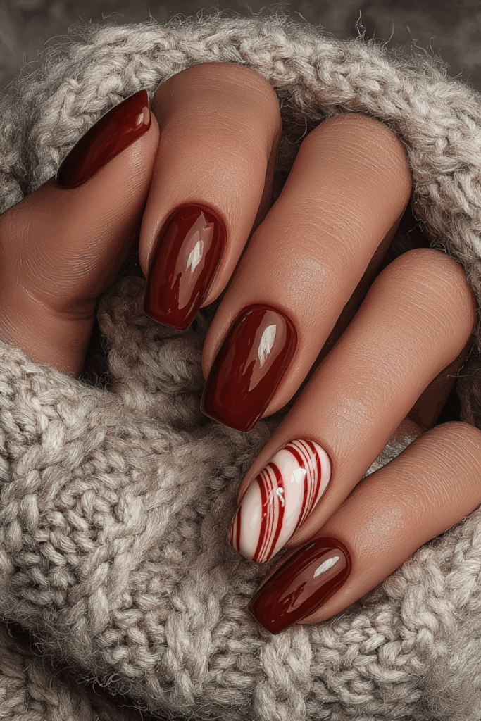 Glossy maroon red almond nails with one accent nail featuring a red and white candy cane striped swirl pattern for Christmas.